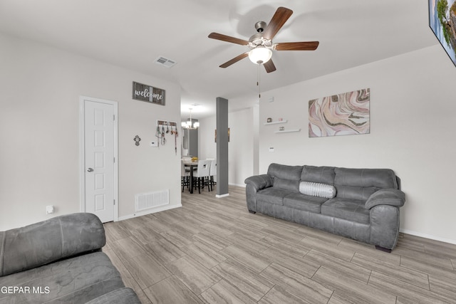 living room with ceiling fan with notable chandelier, baseboards, visible vents, and wood tiled floor