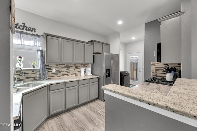 kitchen featuring stainless steel fridge, decorative backsplash, light stone counters, gray cabinetry, and a sink