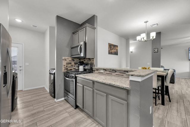 kitchen with washer and clothes dryer, gray cabinets, backsplash, appliances with stainless steel finishes, and a peninsula