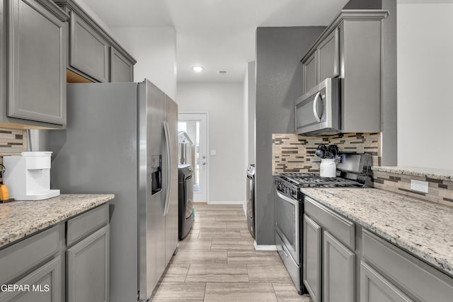 kitchen featuring appliances with stainless steel finishes, independent washer and dryer, gray cabinets, and tasteful backsplash