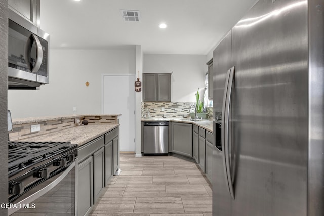 kitchen with visible vents, backsplash, gray cabinetry, appliances with stainless steel finishes, and a sink