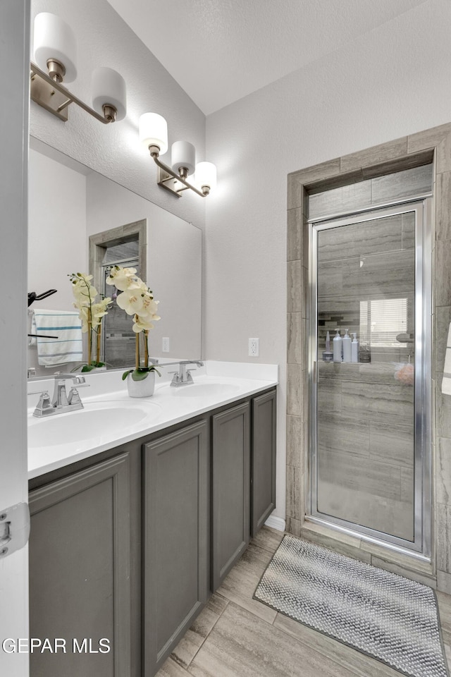 bathroom featuring a textured ceiling, double vanity, a sink, and a shower stall