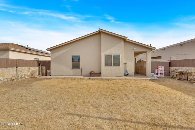 back of property featuring an outbuilding, a storage shed, a lawn, stucco siding, and a patio area