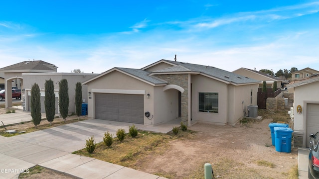 single story home featuring driveway, a garage, stone siding, central air condition unit, and stucco siding