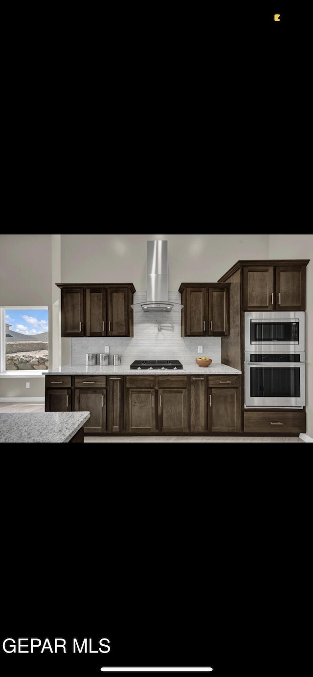 kitchen featuring wall chimney range hood, appliances with stainless steel finishes, decorative backsplash, and dark brown cabinets