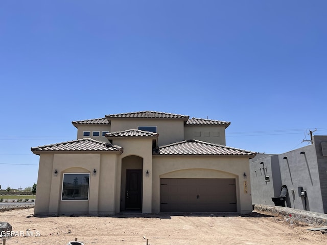 mediterranean / spanish home with a tiled roof, an attached garage, dirt driveway, and stucco siding
