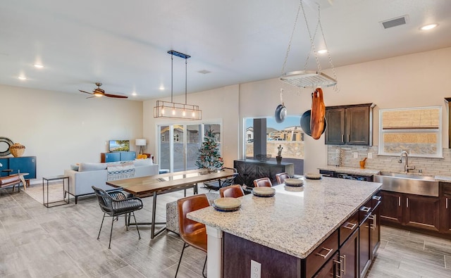 kitchen featuring light stone counters, a kitchen island, a sink, dark brown cabinets, and backsplash