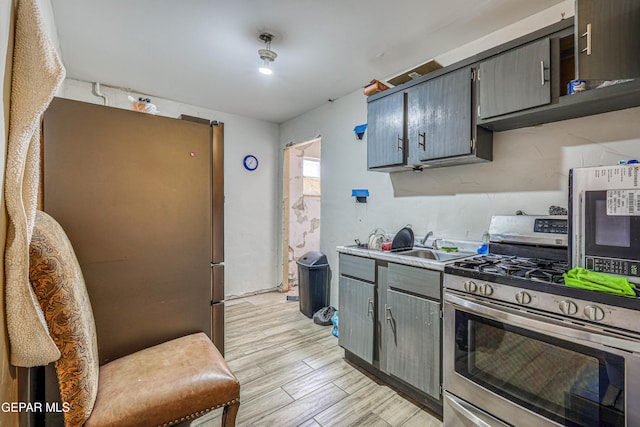 kitchen featuring light countertops, light wood-style flooring, gray cabinetry, appliances with stainless steel finishes, and a sink