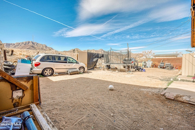 view of yard featuring a trampoline, fence, and a mountain view