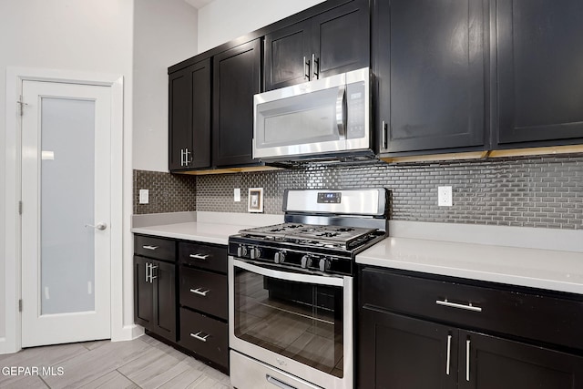 kitchen featuring stainless steel appliances, backsplash, light countertops, and dark cabinets