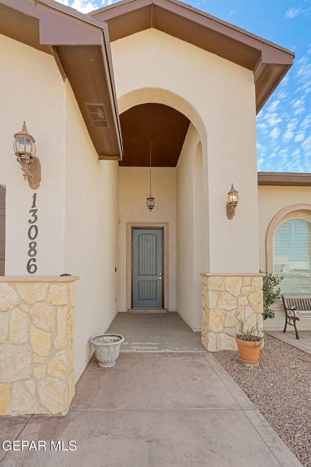 entrance to property with stone siding, visible vents, and stucco siding