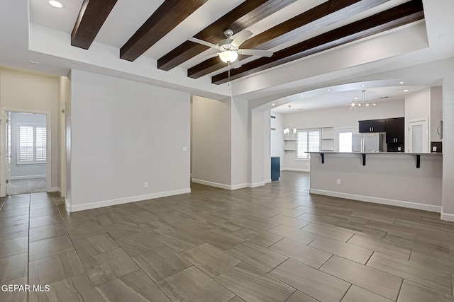 unfurnished living room featuring ceiling fan with notable chandelier, recessed lighting, beam ceiling, and baseboards