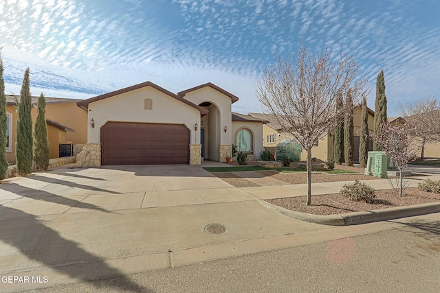 mediterranean / spanish house with a garage, stone siding, driveway, and stucco siding