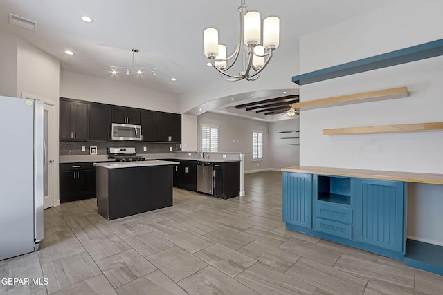 kitchen with a center island, open shelves, stainless steel appliances, decorative backsplash, and ceiling fan with notable chandelier