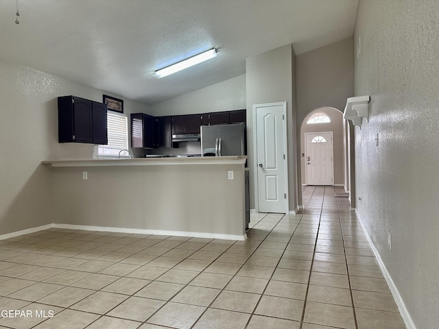 kitchen featuring lofted ceiling, a textured wall, freestanding refrigerator, light tile patterned flooring, and a peninsula