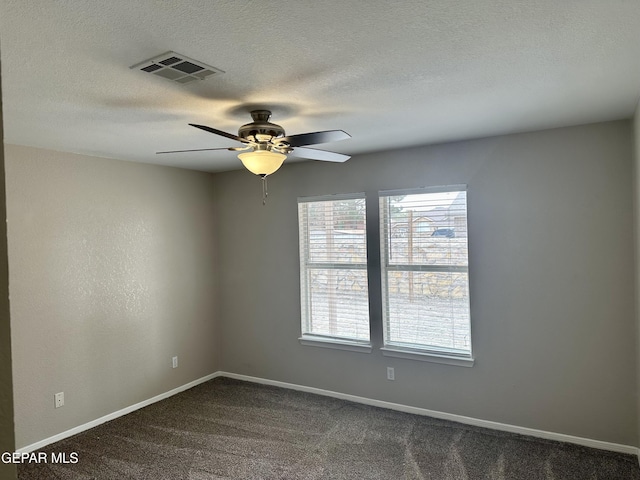 empty room featuring a textured ceiling, dark carpet, visible vents, and baseboards