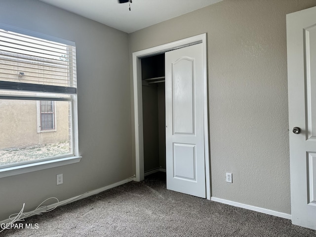 unfurnished bedroom featuring a textured wall, a closet, dark carpet, and baseboards