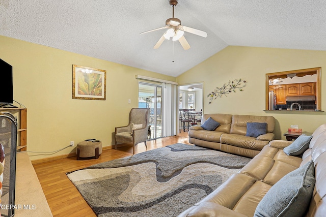 living area with light wood finished floors, lofted ceiling, a ceiling fan, a textured ceiling, and baseboards