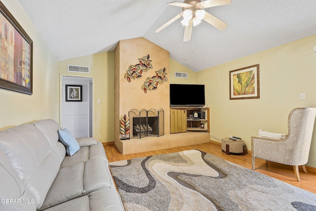 living room with lofted ceiling, visible vents, a fireplace with raised hearth, and wood finished floors