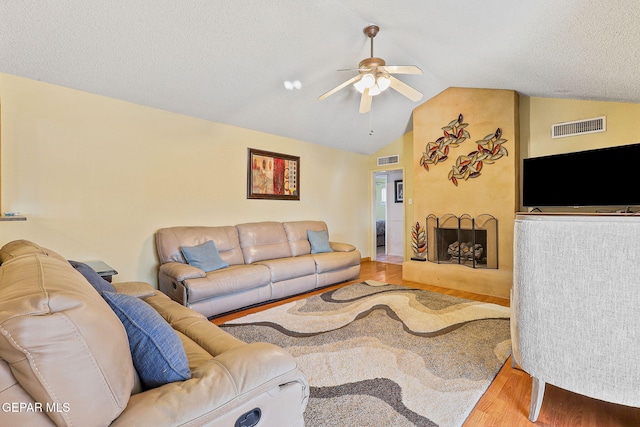 living area with a large fireplace, visible vents, ceiling fan, wood finished floors, and vaulted ceiling