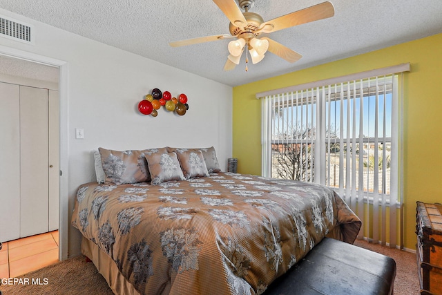 carpeted bedroom featuring a ceiling fan, visible vents, a textured ceiling, and tile patterned floors