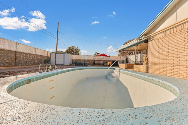 view of swimming pool with fence, a storage unit, and an outbuilding