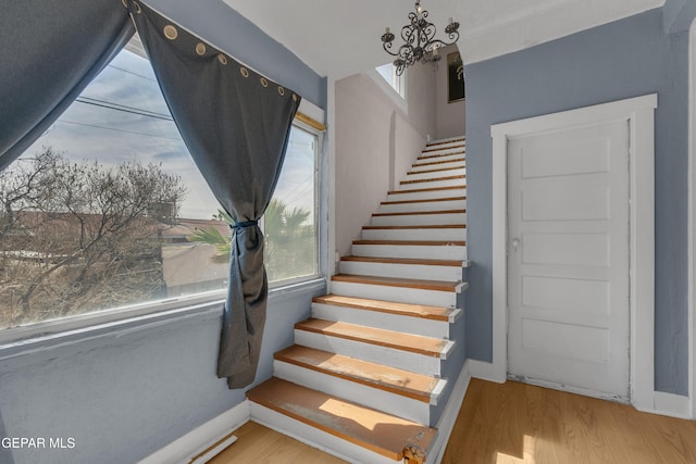 stairs featuring baseboards, a chandelier, and wood finished floors