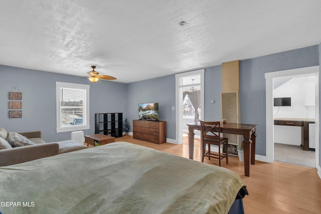 bedroom featuring baseboards, light wood-style flooring, a textured ceiling, and an inviting chandelier