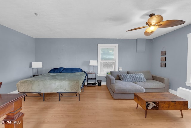 bedroom with light wood-style floors, radiator, baseboards, and a ceiling fan