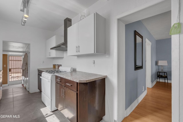 kitchen with white range with gas cooktop, white cabinets, light wood-style floors, light countertops, and wall chimney range hood