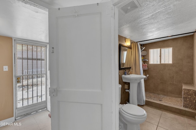 full bath with visible vents, toilet, a tile shower, a textured ceiling, and tile patterned floors