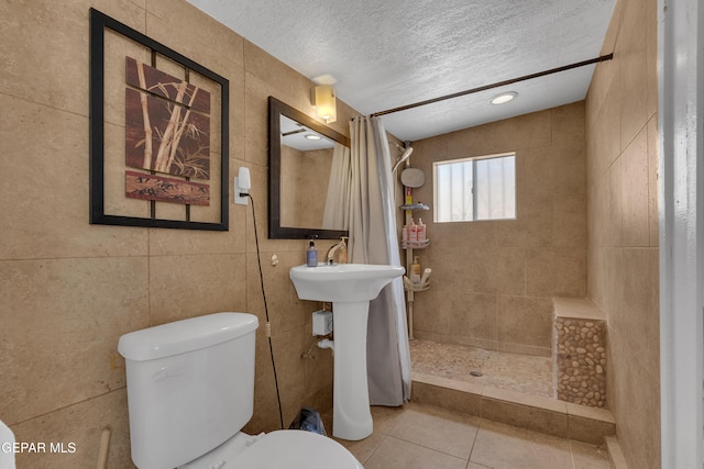 bathroom with tile walls, toilet, a textured ceiling, tile patterned flooring, and tiled shower