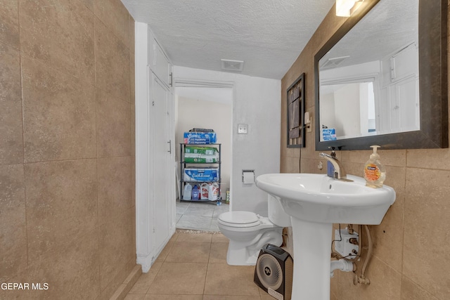 bathroom with tile walls, visible vents, toilet, a textured ceiling, and tile patterned flooring