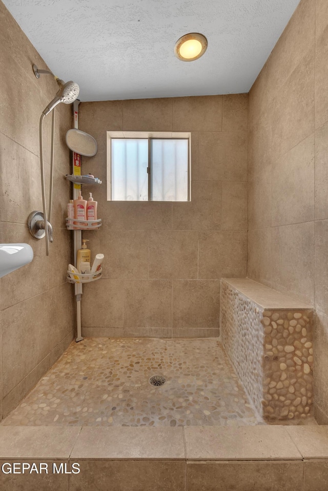 full bath featuring a textured ceiling and a tile shower