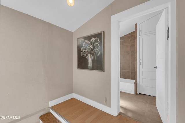 hall featuring baseboards, vaulted ceiling, and wood finished floors