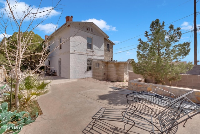 back of property featuring a patio area, brick siding, a chimney, and fence