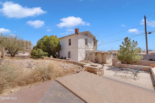 view of side of property with a chimney, a patio, fence, and stucco siding