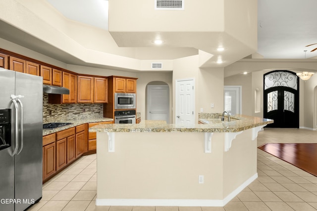 kitchen featuring arched walkways, light tile patterned flooring, stainless steel appliances, visible vents, and a kitchen breakfast bar