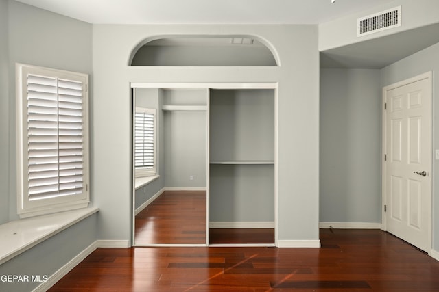 unfurnished bedroom featuring baseboards, a closet, visible vents, and wood finished floors