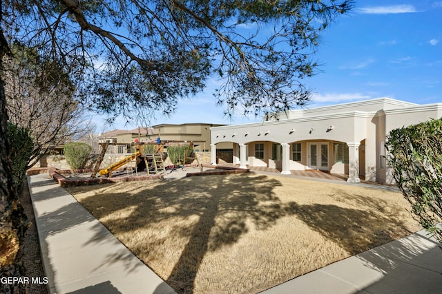 view of front of home with stucco siding, a playground, and french doors