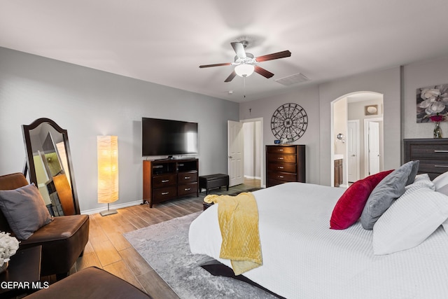 bedroom featuring visible vents, arched walkways, connected bathroom, baseboards, and light wood-type flooring