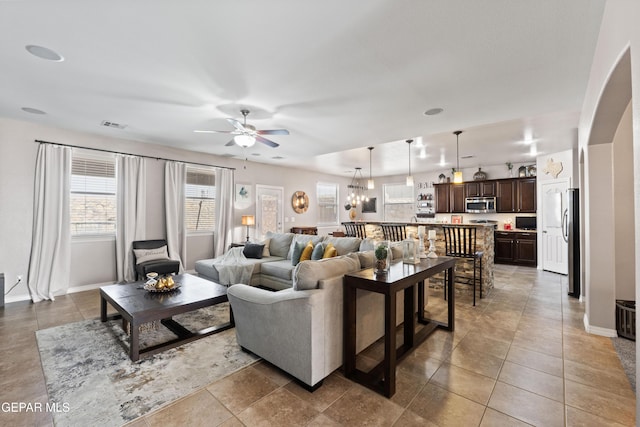 tiled living area featuring arched walkways, visible vents, baseboards, and ceiling fan with notable chandelier