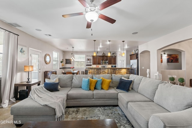 living room with arched walkways, ceiling fan, and visible vents