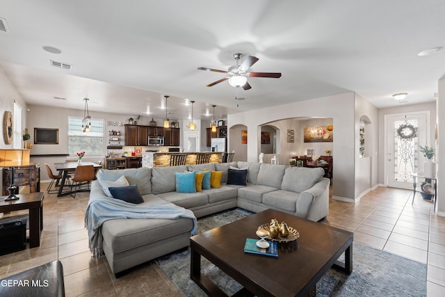 living area with light tile patterned floors, visible vents, arched walkways, baseboards, and ceiling fan