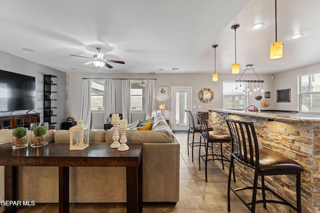 living room featuring light tile patterned floors, bar, and a ceiling fan