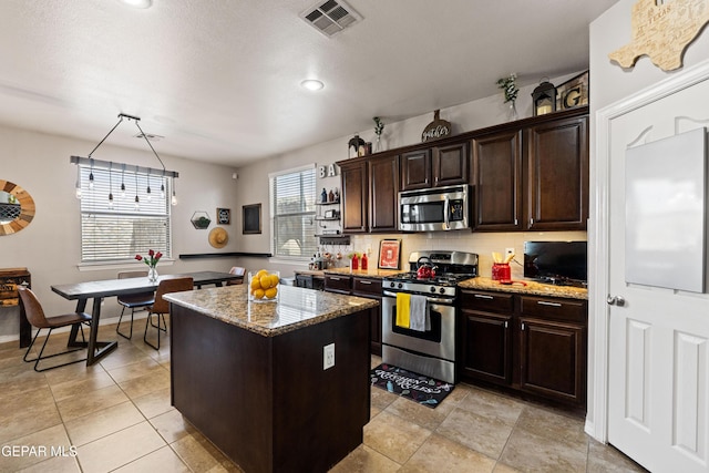 kitchen featuring light stone counters, stainless steel appliances, a kitchen island, visible vents, and tasteful backsplash