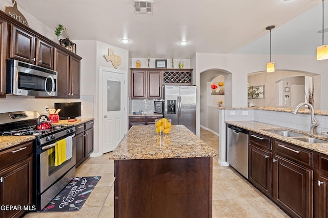 kitchen featuring stainless steel appliances, a kitchen island, a sink, visible vents, and decorative light fixtures