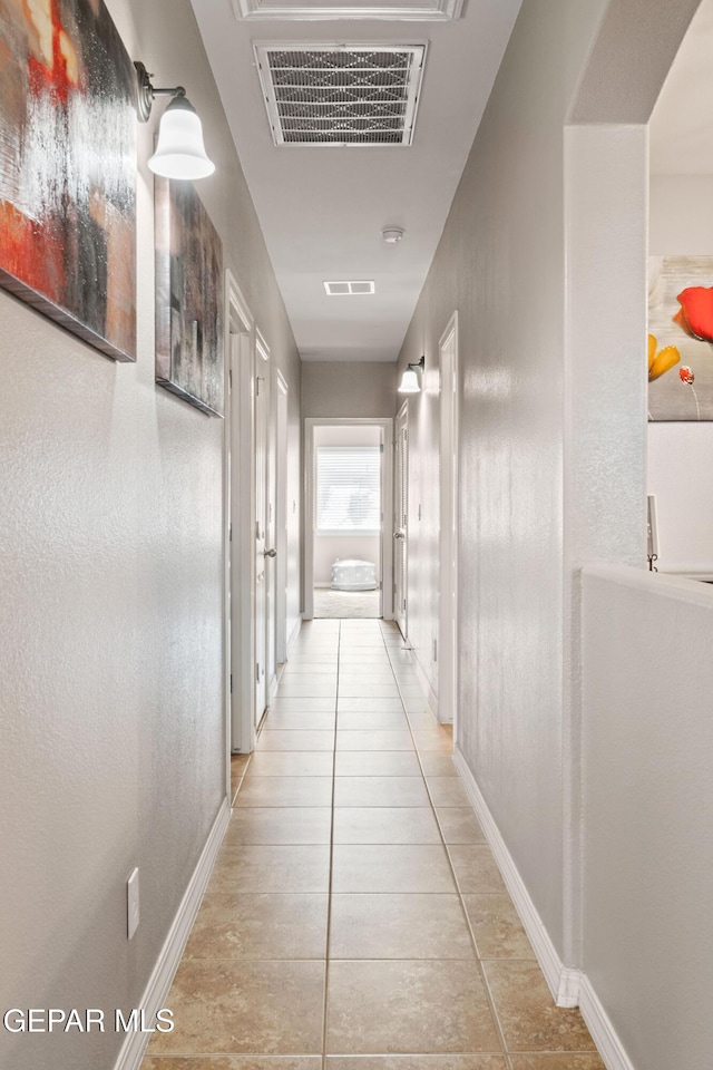 hall featuring light tile patterned floors, visible vents, and baseboards