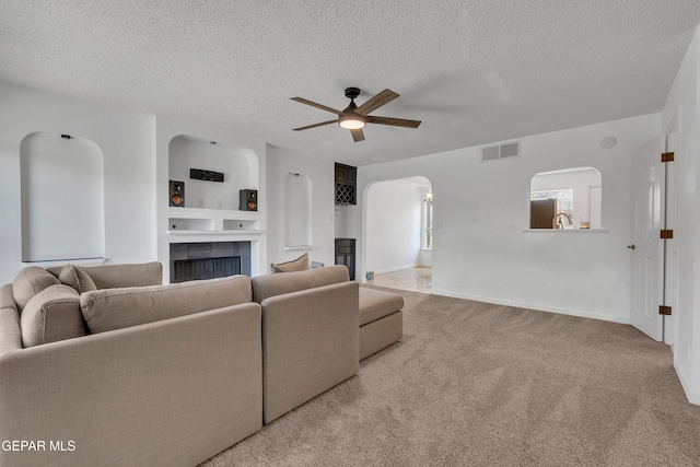 living room featuring light colored carpet, visible vents, a fireplace, and a textured ceiling