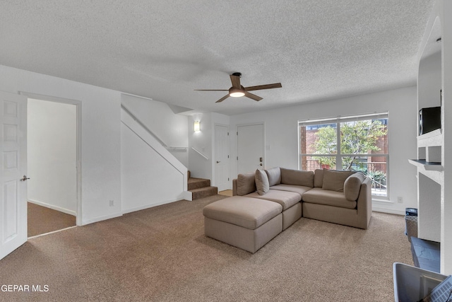 living area with light colored carpet, ceiling fan, stairs, a textured ceiling, and a brick fireplace